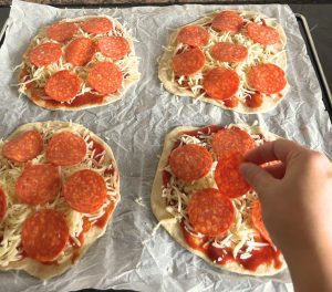 Mão a colocar ingredientes em mini pizzas caseiras durante um momento de mindfulness ativo.